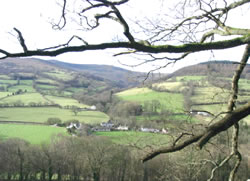 View of the meadows and pastures in the valley below, with the hills of the Brecon Beacons in the background